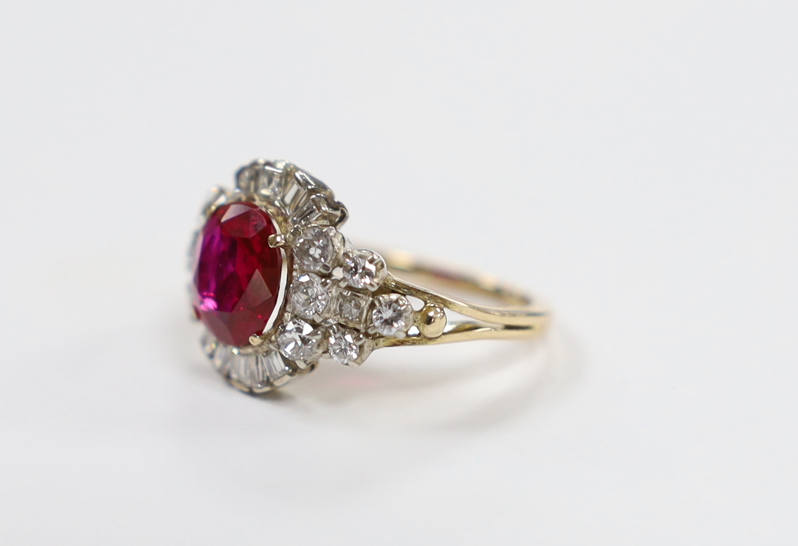 A yellow metal, singe stone round cut synthetic ruby and diamond set circular cluster dress ring, with diamond set shoulders, size J/K, gross weight 4.3 grams.